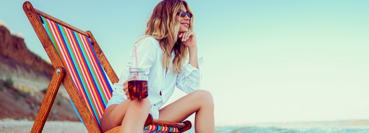 Brunette woman sitting on a striped beach chair looking at ocean